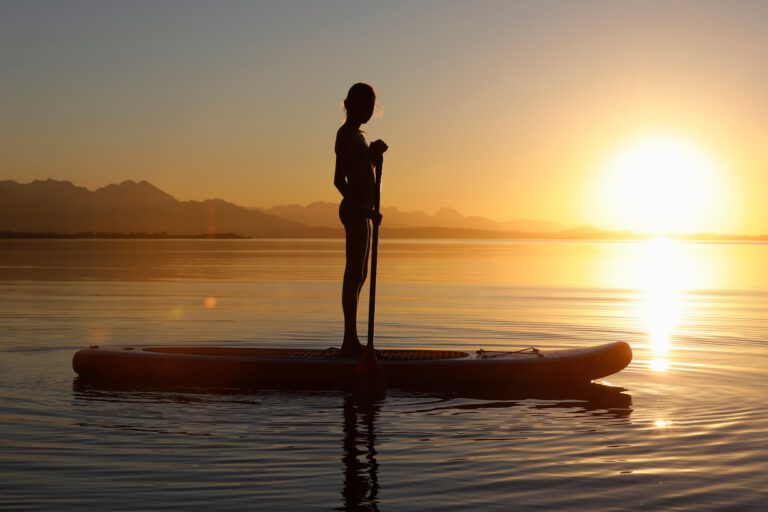 Young girl paddle boarding on water, at sunset