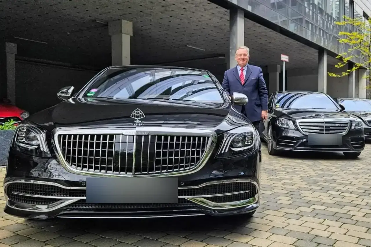 Chauffeur im Anzug neben einer Mercedes-Maybach S-Klasse, dahinter weitere Limousinen