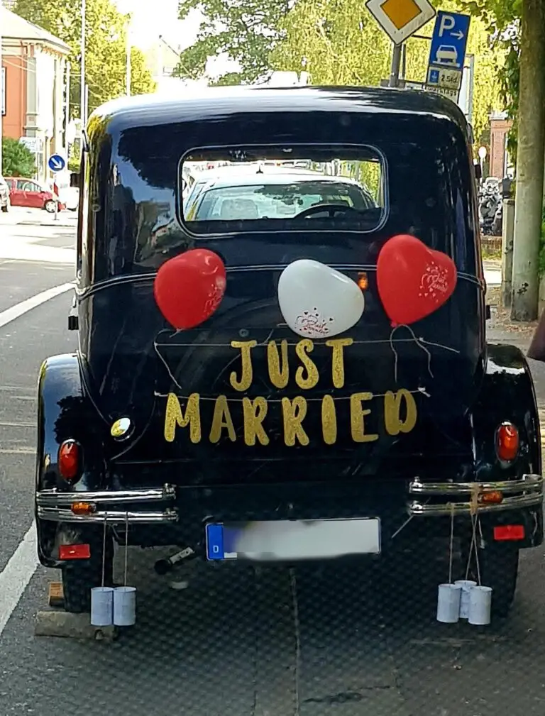 Hochzeitsauto mit Aufschrift Just Married, Herzballons und Dosen am Heck