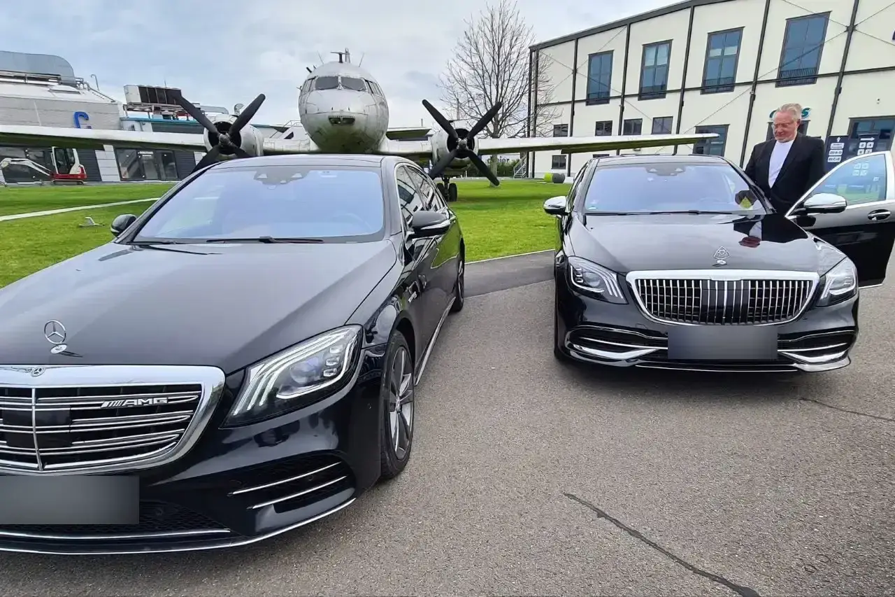 Chauffeur an einer Mercedes-Maybach S-Klasse, links eine Mercedes S-Klasse, im Hintergrund ein historisches Flugzeug
