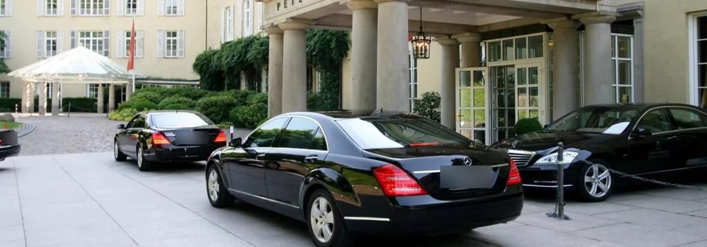 Drei schwarze Mercedes-Limousinen in der Vorfahrt eines Grandhotels